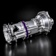 A polished metallic automotive transmission or torque converter component photographed on a dark reflective studio surface. A purple band wraps around part of the unit, and a visible logo reads PRB Performance.