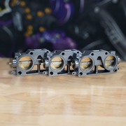 Three metallic throttle bodies on a wooden surface with a blurred background