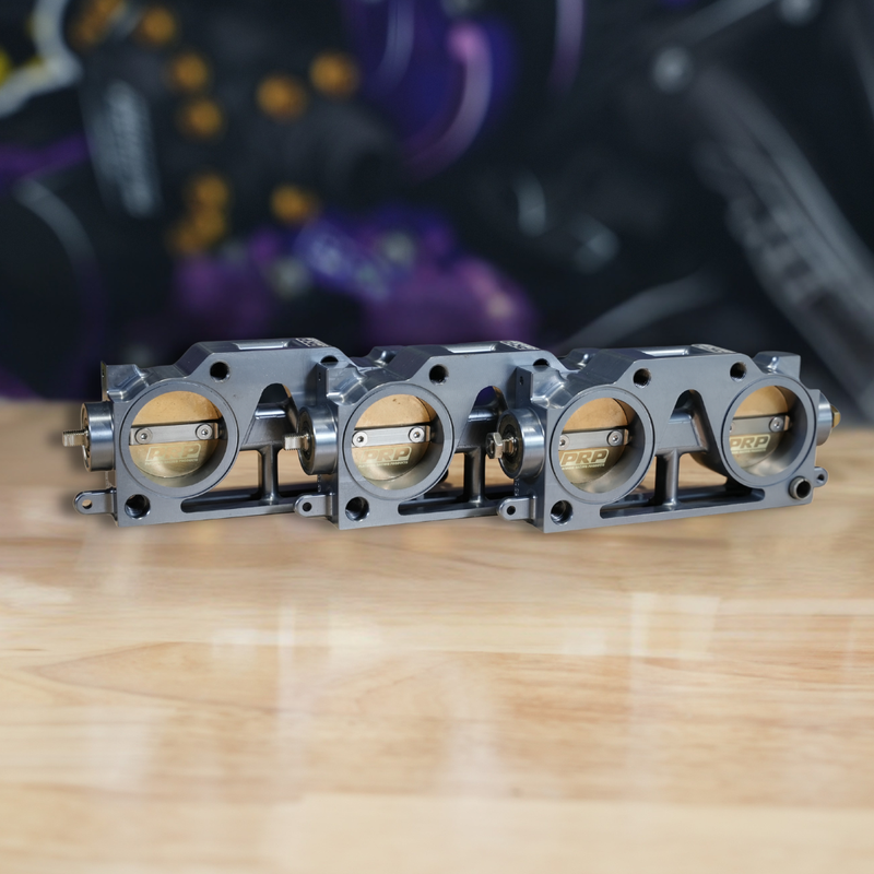 Three metallic throttle bodies on a wooden surface with a blurred background