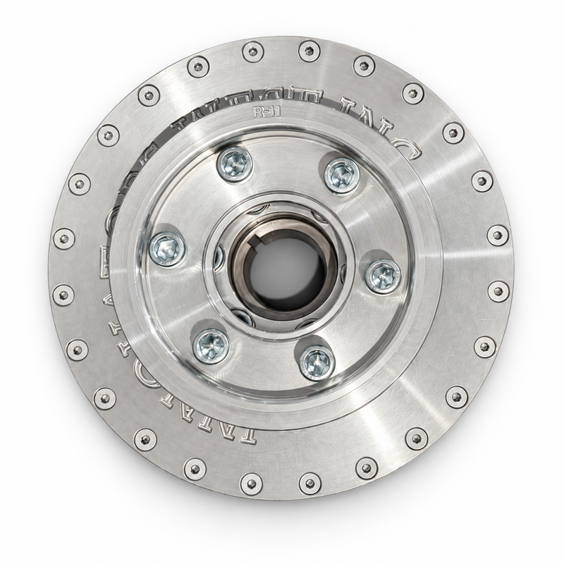 A polished metallic circular mechanical component, likely a clutch plate or flywheel, featuring a central hub with six bolt holes and a flange rim with evenly spaced rivets and engraved text.